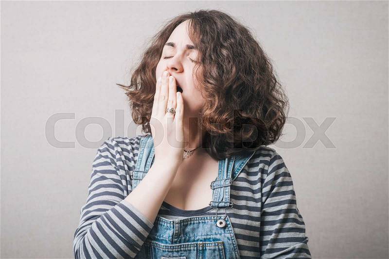 The woman yawns. On a gray background, stock photo