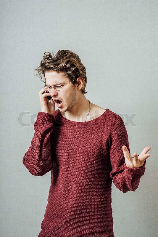 The man speaks on the phone cursing. On a gray background, stock photo
