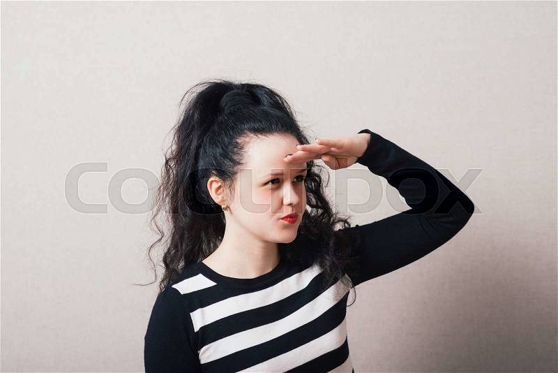 Woman looking into the distance hand near head. Gray background, stock photo