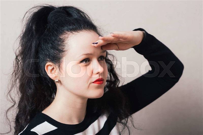 Woman looking into the distance hand near head. Gray background, stock photo