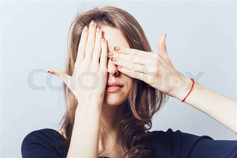 Young teen woman covering her eyes isolated on a gray background, stock photo
