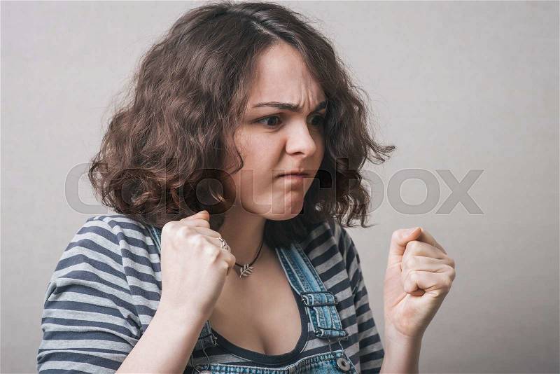 Angry woman threatening the fist over grey background, stock photo