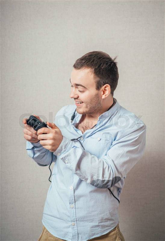 Happy young man in winning pose wearing shirt holding video game joystick, stock photo