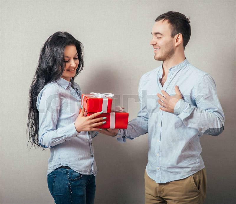 Girl is giving a gift to her boyfriend. Isolated on a gray background, stock photo