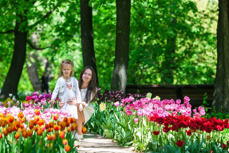 Adorable little girl and young mom enjoying warm day in tulip garden, stock photo