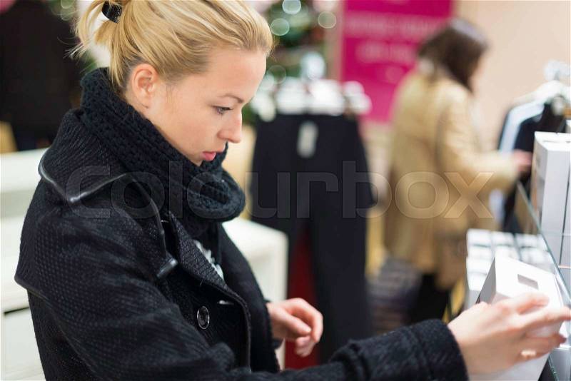Woman shopping lingerie . Shopper looking and choosing clothing indoors in store. Beautiful blonde caucasian female model wearing winter coat and fashionable knitted cap, stock photo