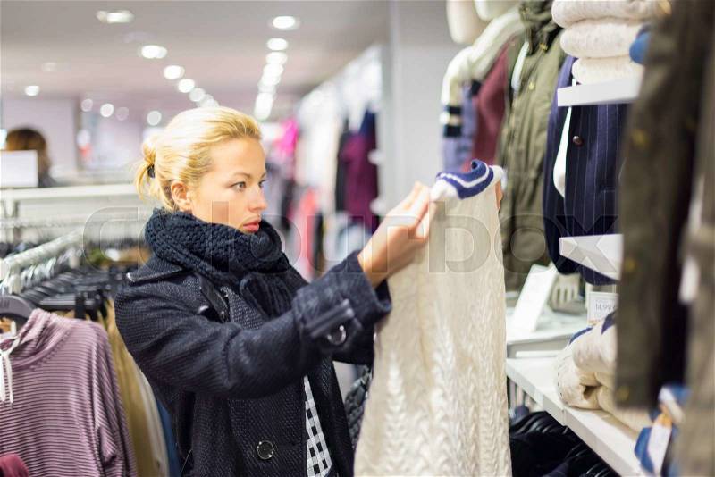 Woman shopping clothes. Shopper looking at clothing indoors in store. Beautiful blonde caucasian female model. , stock photo