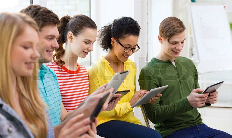 Education, technology and internet concept - smiling students looking at tablet pc computer at school, stock photo