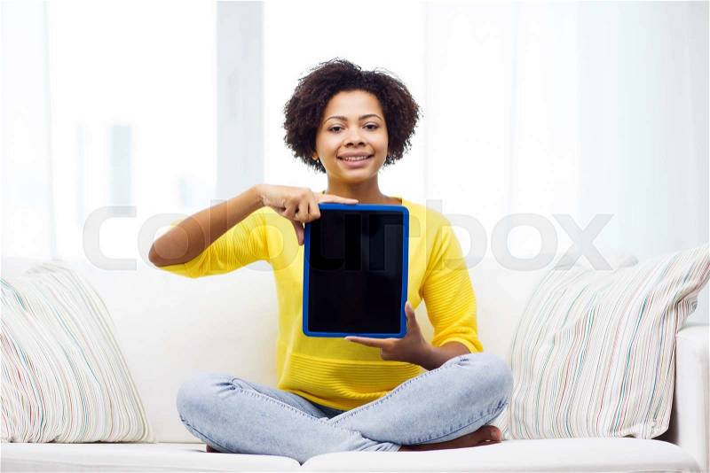 People, technology, advertisement and leisure concept - happy african american young woman sitting on sofa and showing tablet pc computer black blank screen at home, stock photo