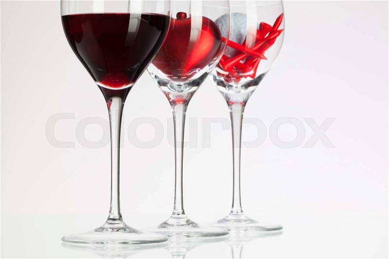 Wine glasses with red wine, heart and golf ball on white table, stock photo