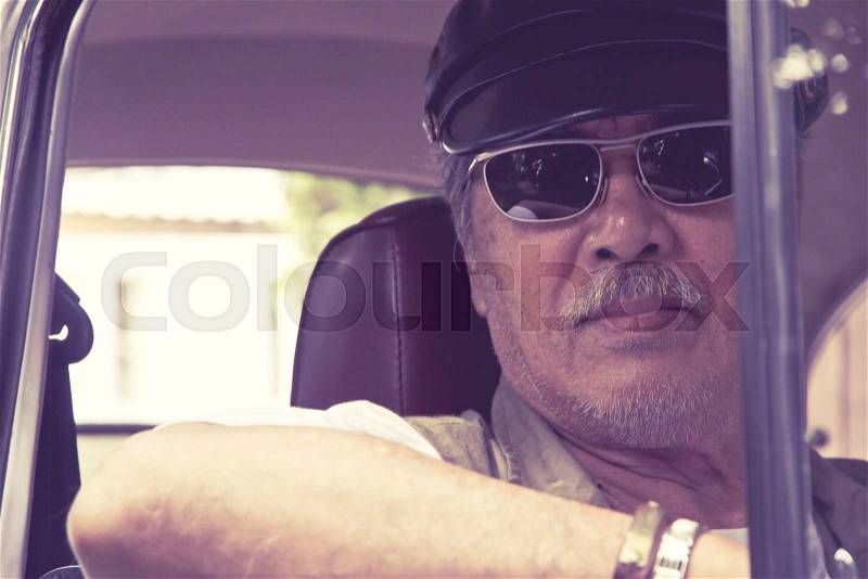 Close up image of older man with glasses driving a car, stock photo