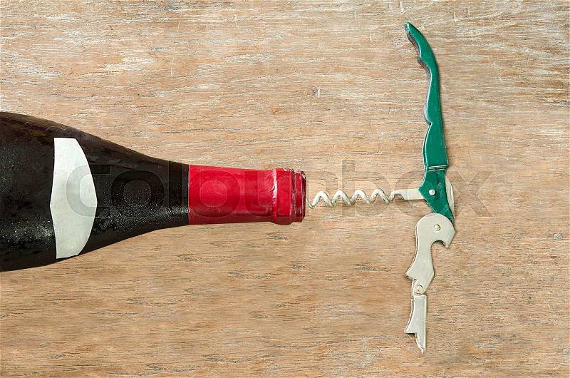 Red wine bottle with opener on wood background, stock photo