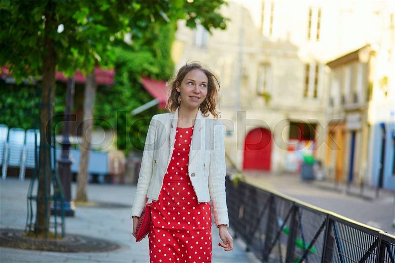 Beautiful young woman in red polka dot dress walking on a street of Marais in Paris, France, stock photo