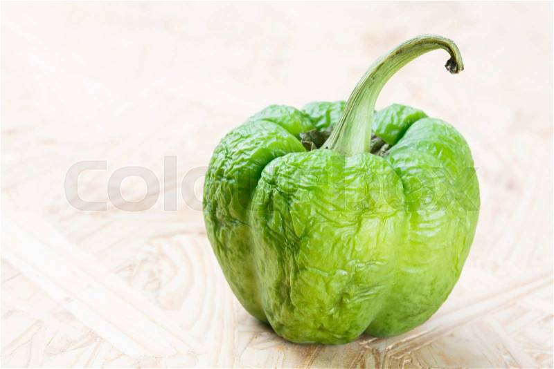 Close up wrinkled green bell pepper on particle board, stock photo