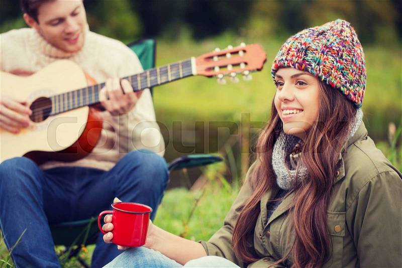 Adventure, travel, tourism and people concept - smiling couple with guitar in camping, stock photo