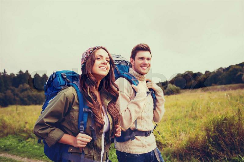 Adventure, travel, tourism, hike and people concept - smiling couple walking with backpacks outdoors, stock photo