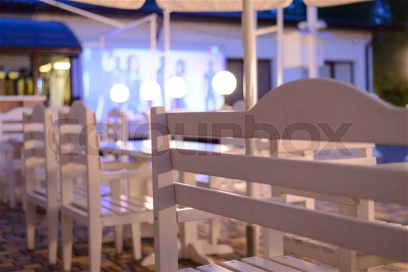 White Tables and Chairs on Outdoor Patio at Night, View of Empty Restaurant or Club Patio from Across Shiny Clean Table Surface, stock photo