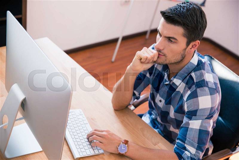 Handsome businessman in casual cloth sitting at the table and using personal computer in office, stock photo
