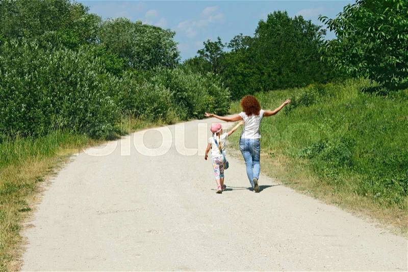 Mother and daughter walking by rural road among trees in lovely summer day, stock photo