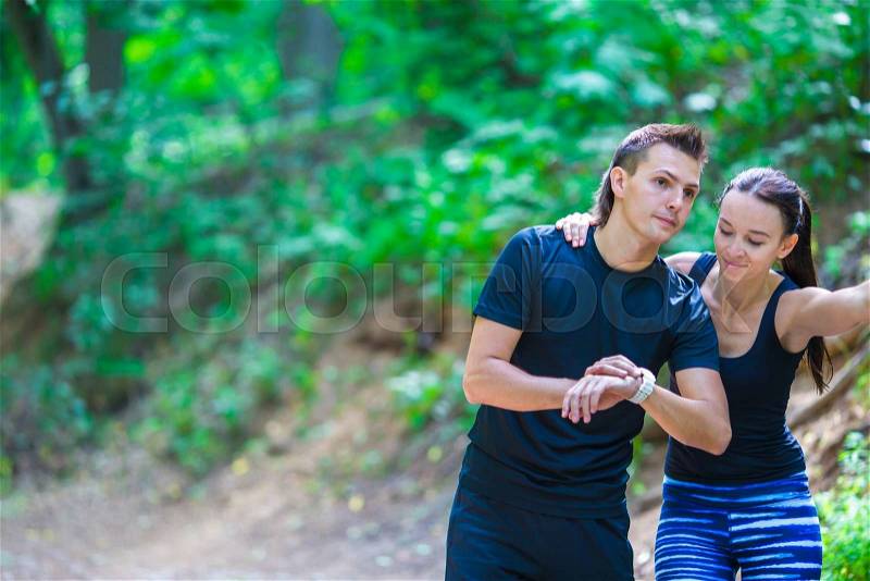 Young active couple looking at smart watch heart rate monitor having break while running at forest, stock photo