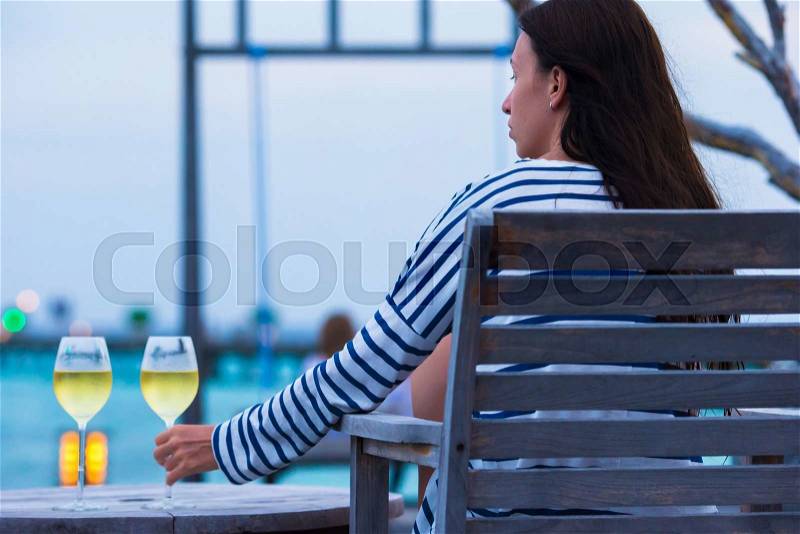 Young girl with glass of white wine at evening outdoor cafe, stock photo