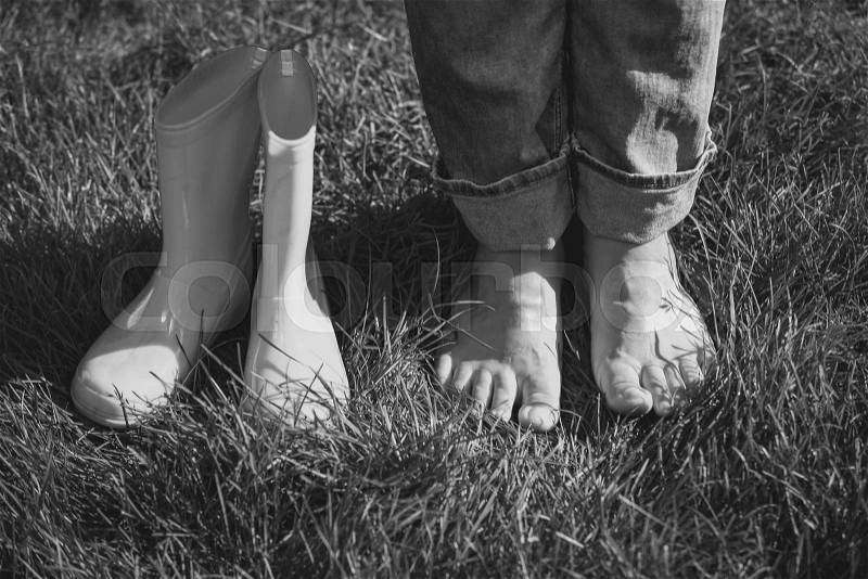Black and white photo of girl took off gumboots and standing on grass, stock photo