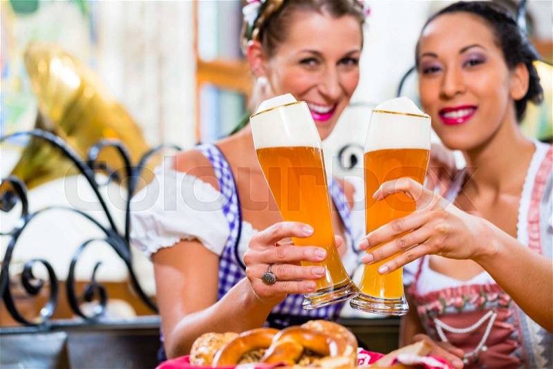 Women in Bavarian pub wearing traditional Tracht toasting with wheat beer, stock photo