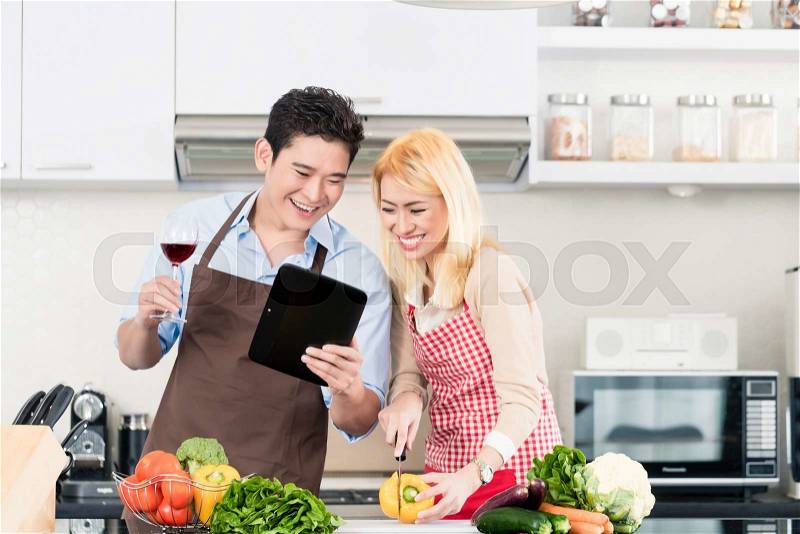 Asian couple cooking after recipes from tablet computer, stock photo