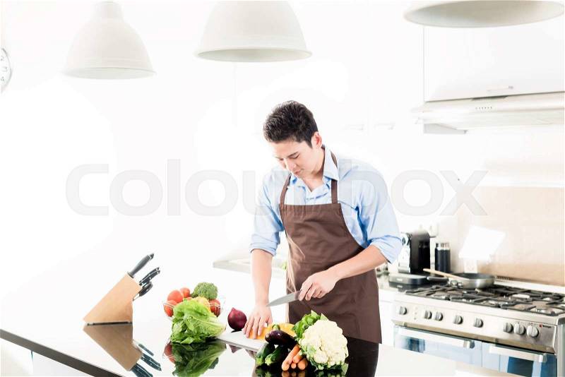 Japanese man cooking food in minimalist kitchen, stock photo