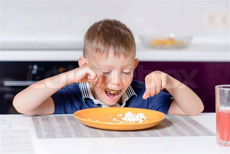 Young Blond Boy Eating Last Bite of Food from Plate While Sitting at Kitchen Table, stock photo