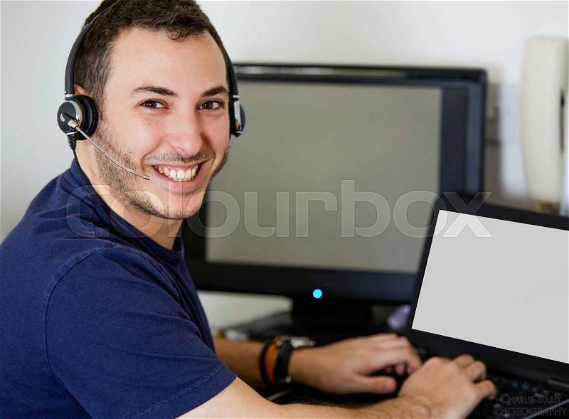 Close up Handsome Call Center Agent Guy Smiling at the Camera While Working on his laptop Computer, stock photo