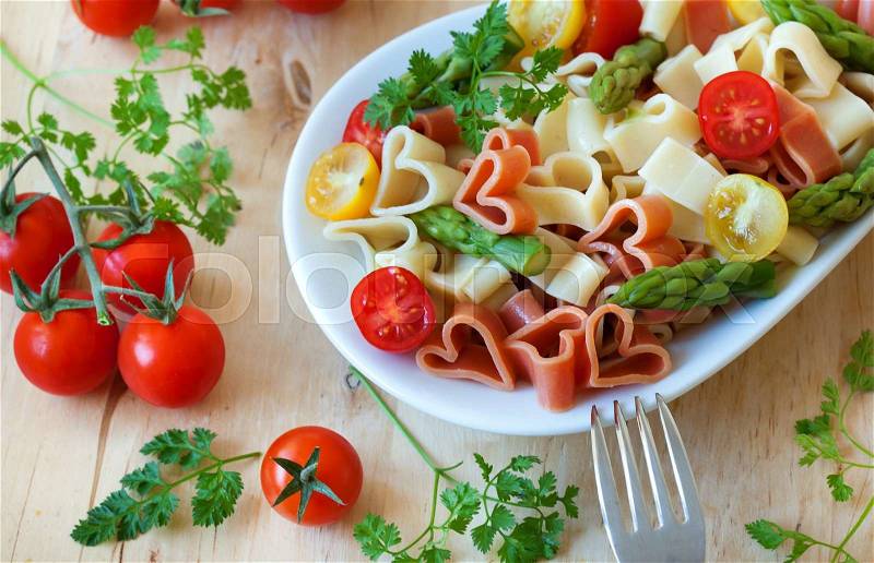 Romantic dinner. Delicious heart-shaped pasta with tomatoes, asparagus and fresh herbs, stock photo