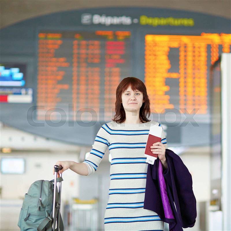 Beautiful young female passenger at the airport in the arrivals-departure hall, holding passport and boarding pass, stock photo