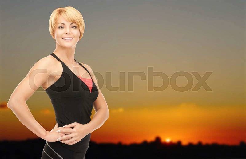 People, fitness and sport concept - happy woman posing outdoors over sunset skyline background, stock photo