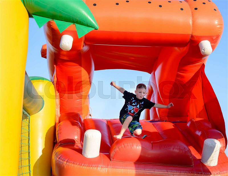 Young boy jumping barefoot on a plastic jumping castle with his arms in the air as he enjoys a summer day at a playground or fair, stock photo