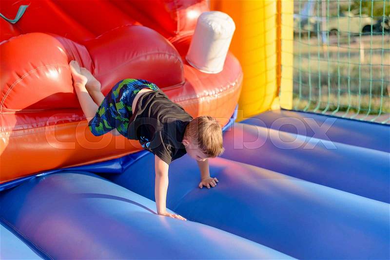 Young boy tumbling around on an inflatable plastic jumping castle in a kids playground or at an annual fair, stock photo