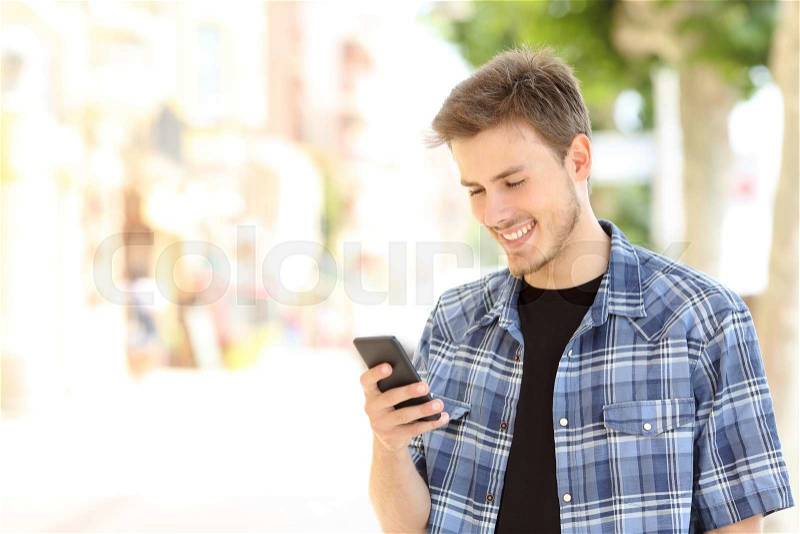 Young casual man using a smart phone texting messages in the street, stock photo