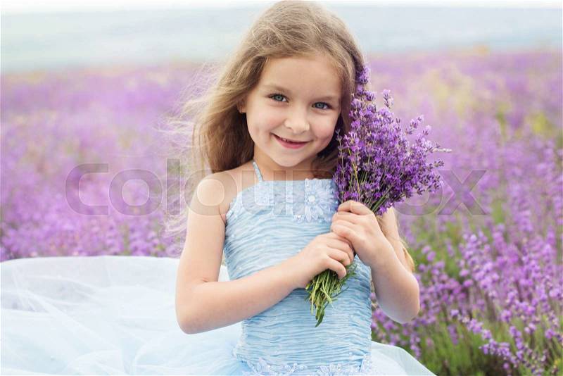 Happy little girl is in a lavender field holding bouquet of flowers, stock photo