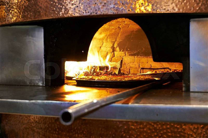 Traditional wood fired pizza being placed into a super hot brick pizza oven. , stock photo