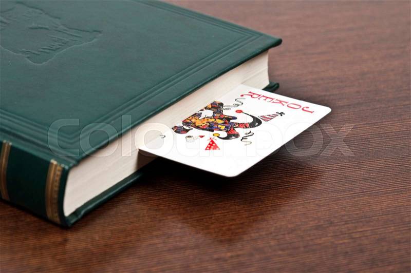 Book and joker card on desk, stock photo