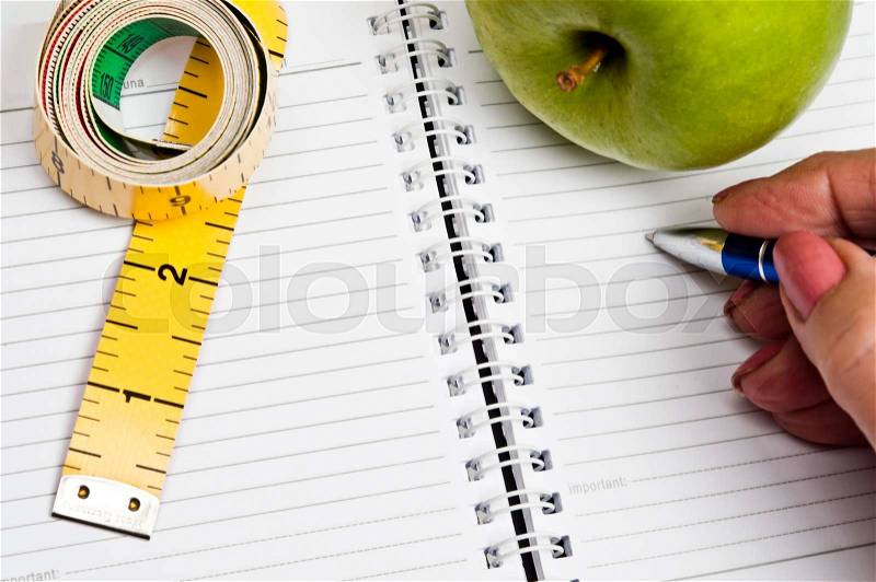 Measurement tape and apple on notebook, stock photo