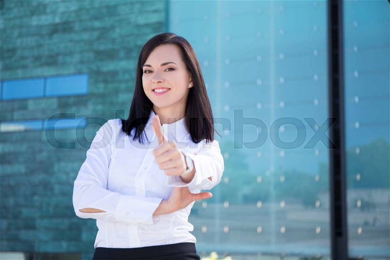Portrait of young business woman thumbs up in street, stock photo