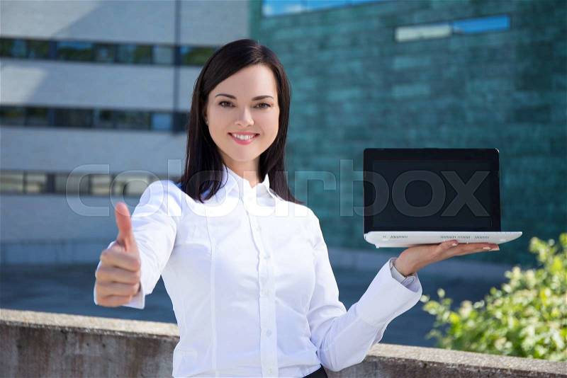 Young beautiful business woman showing laptop with blank screen and thumbs up, stock photo
