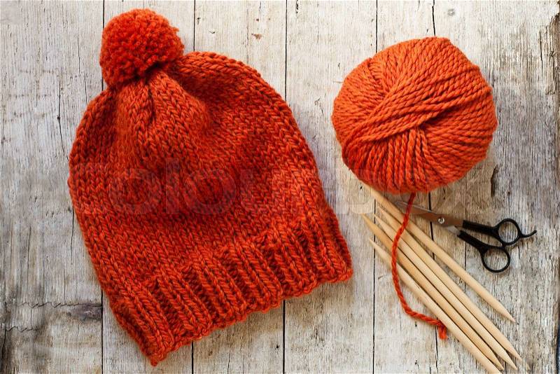 Wool orange hat, knitting needles and yarn on wooden background, stock photo