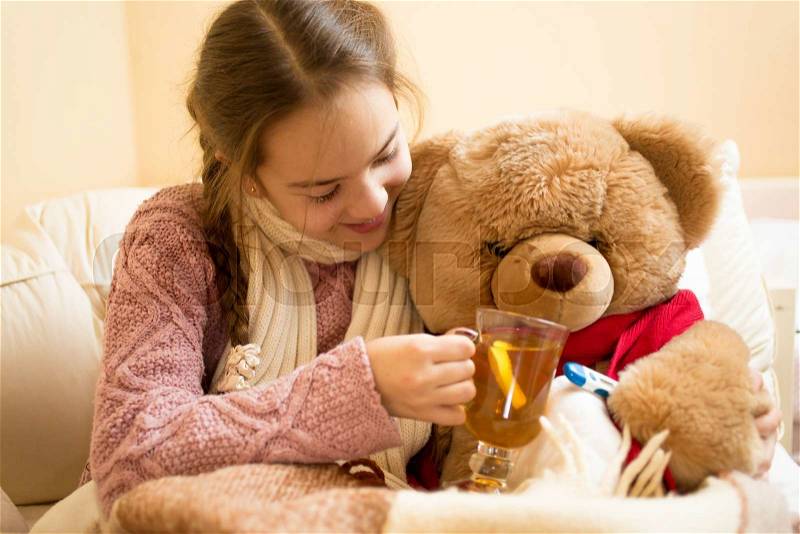 Closeup photo of little sick girl giving hot tea to teddy bear, stock photo