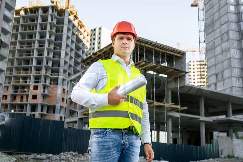 Portrait of architect in red hardhat posing on building site, stock photo