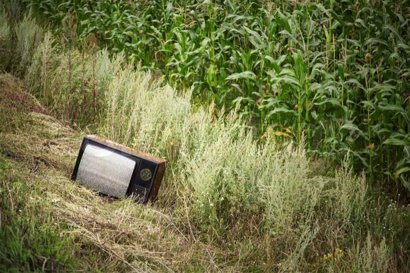 Old broken TV in the field with white noise on screen, stock photo