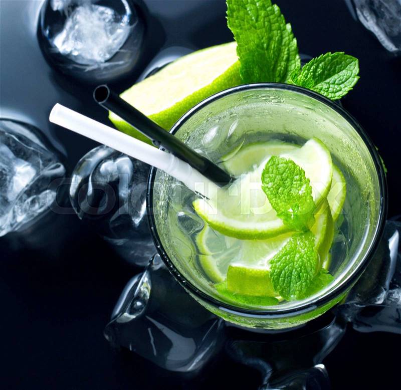 Cold Mojito cocktail with fresh lime, mint and ice on black table, stock photo
