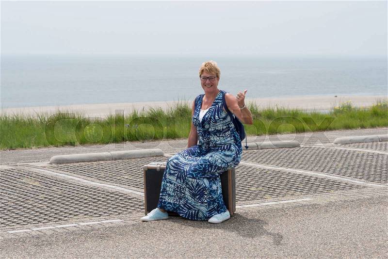 Woman sitting on old suitcase and travel alomng the beach by hitchhiking, stock photo