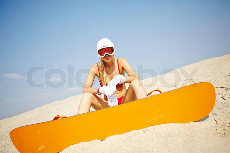 Active young sandboarder in red bikini sitting on sand, stock photo